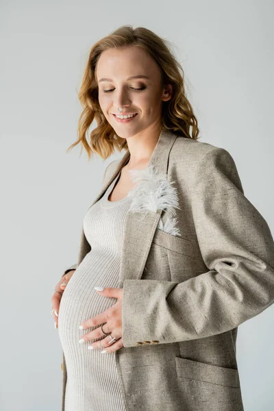 Portrait of fashionable pregnant woman in jacket standing isolated on grey — Stock Photo