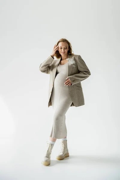 Full length of fashionable pregnant woman in boots and dress standing on grey background — Stock Photo