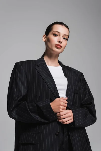 Низький кут зору стильної жінки в куртці, що стоїть ізольовано на сірому — стокове фото
