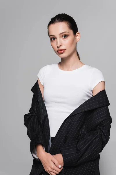 Modelo na moda jovem em terno preto e camiseta olhando para a câmera isolada em cinza — Fotografia de Stock