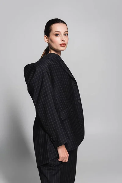 Stilvolles brünettes Modell im schwarzen Anzug mit Blick auf die Kamera auf grauem Hintergrund — Stockfoto