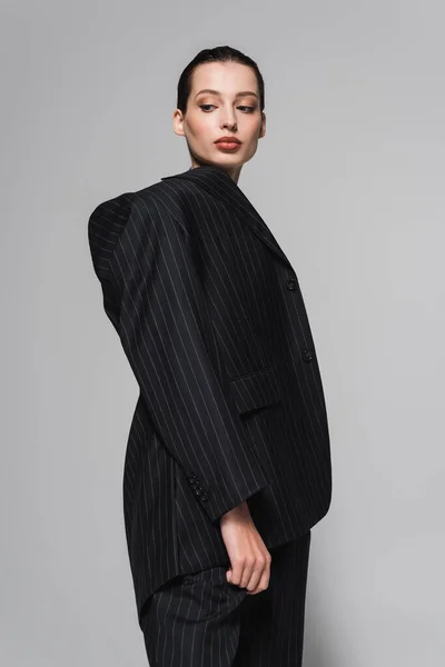 Tiefansicht einer hübschen Frau im schwarzen Anzug, die isoliert von Grau wegschaut — Stockfoto