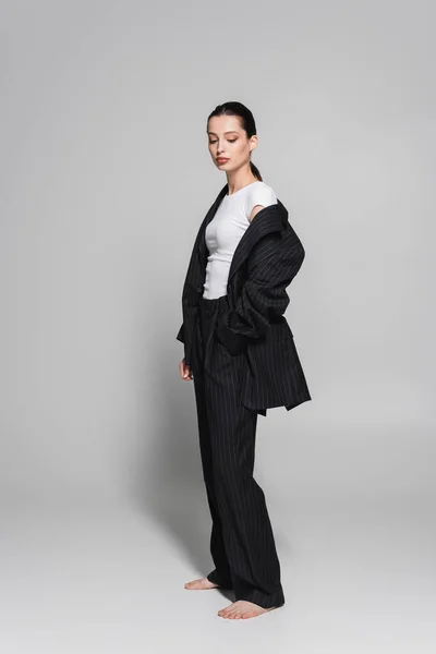 Piena lunghezza della donna alla moda in abito in piedi su sfondo grigio — Foto stock