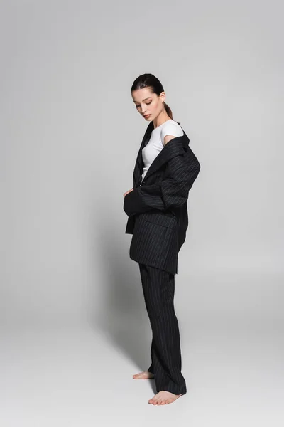Модель босоніж в чорному костюмі, що стоїть на сірому фоні з тіні — стокове фото