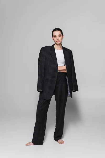 Full length of barefoot model in suit posing on grey background — Stock Photo