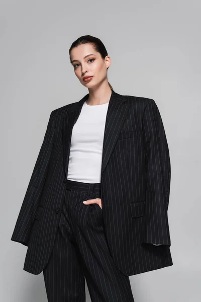 Trendige junge Frau im gestreiften Anzug posiert isoliert auf grau — Stockfoto