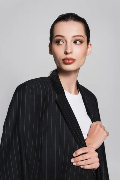 Портрет жінки в футболці і смугастій куртці, що дивиться ізольовано на сірому — стокове фото