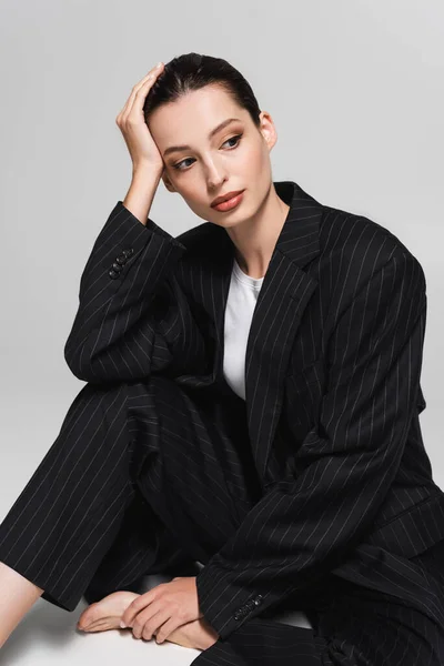 Schöne brünette Frau im Anzug sitzt auf grauem Hintergrund — Stockfoto