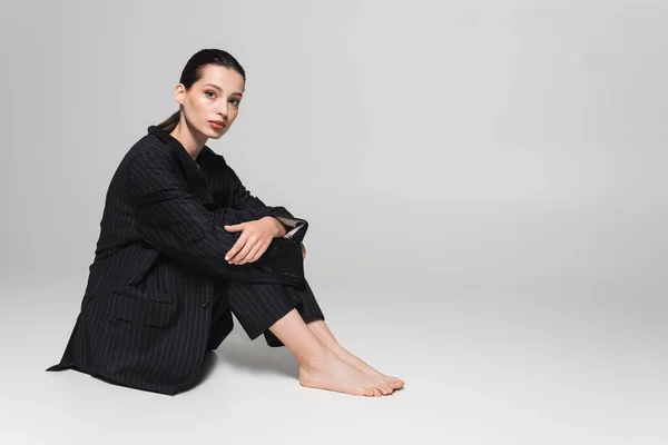 Elegante jovem mulher de terno preto sentado no fundo cinza — Fotografia de Stock