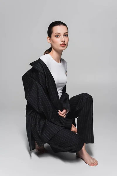 Модна і босоніж модель в костюмі позує на сірому фоні — стокове фото