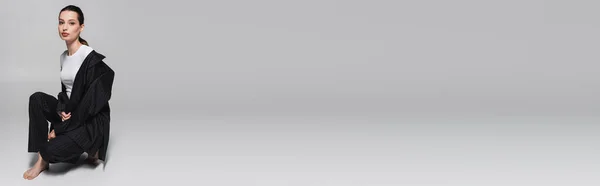 Модель Брюнета в футболці і костюм, дивлячись на камеру на сірому фоні, банер — стокове фото