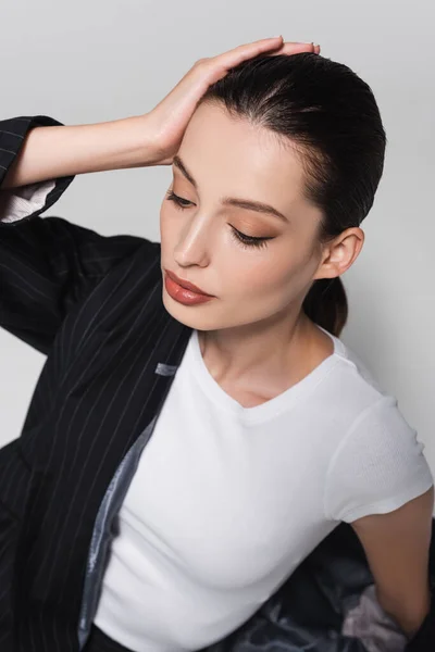High angle view of brunette model in t-shirt and jacket touching hair isolated on grey — Stock Photo