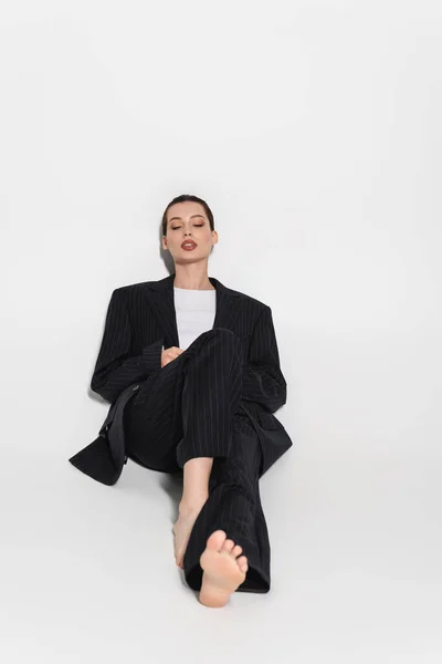 Elegante modelo descalço em terno deitado sobre fundo cinza — Fotografia de Stock
