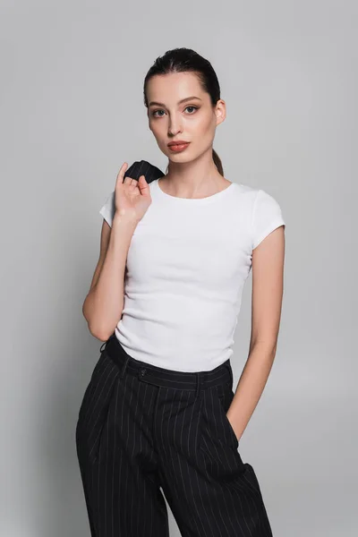 Trendy young woman in t-shirt holding jacket on grey background — Stock Photo