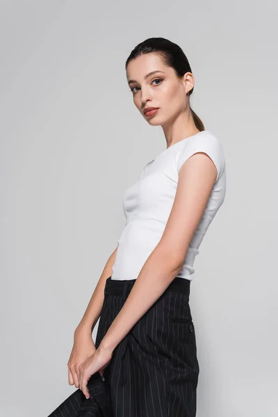 Stilvolle Frau in weißem T-Shirt mit Jacken-Werbung und Blick in die Kamera vereinzelt auf grau — Stockfoto