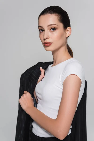 Портрет жінки в футболці позує з смугастим піджаком ізольовано на сірому — стокове фото