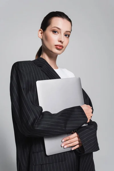 Портрет молодої жінки в смугастій куртці, що тримає ноутбук ізольовано на сірому — стокове фото