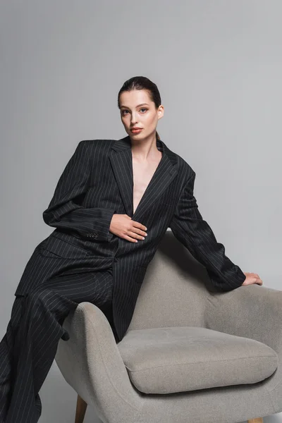 Modische Frau im Anzug posiert neben Sessel auf grauem Hintergrund — Stockfoto