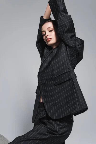 Trendy junge Frau mit Make-up im schwarzen Anzug posiert isoliert auf grau — Stockfoto