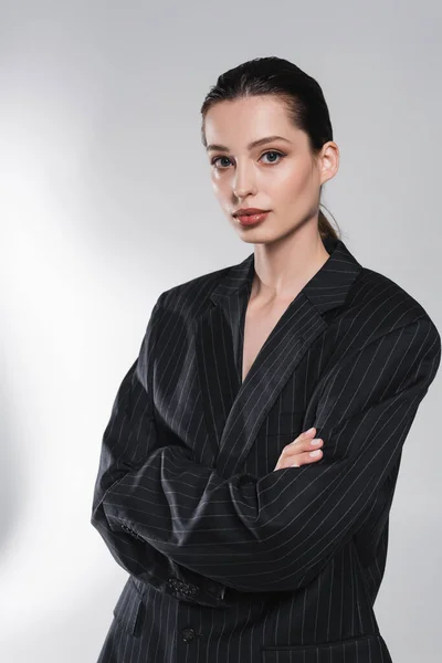 Модная женщина в черной куртке скрещивает руки на абстрактном сером фоне — стоковое фото