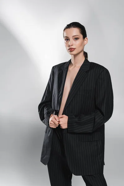 Mulher na moda em jaqueta listrada olhando para a câmera no fundo cinza abstrato — Fotografia de Stock