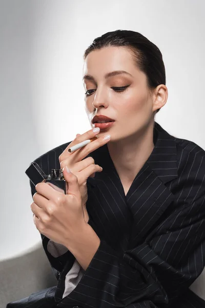 Junge Frau in gestreifter Jacke mit Feuerzeug und Zigarette auf grauem Hintergrund — Stockfoto