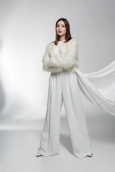 Donna in abiti bianchi e giacca di pelliccia sintetica con abbigliamento in posa su sfondo grigio astratto — Foto stock