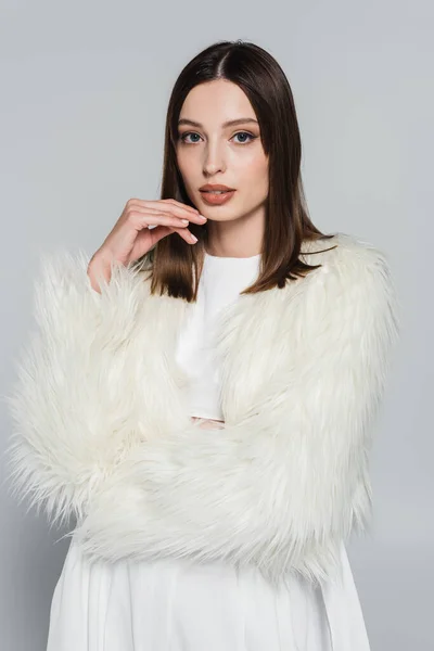 Retrato de mulher muito jovem na elegante jaqueta de pele de falso branco olhando para a câmera isolada no cinza — Fotografia de Stock