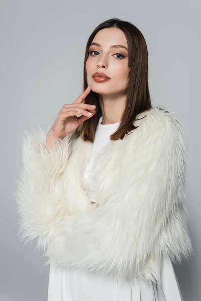 Ritratto di giovane donna alla moda in elegante giacca di eco pelliccia bianca guardando la fotocamera isolata sul grigio — Foto stock
