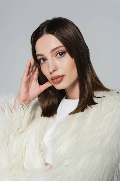 Retrato de mulher bonita na elegante jaqueta de pele de falso branco olhando para a câmera isolada no cinza — Fotografia de Stock