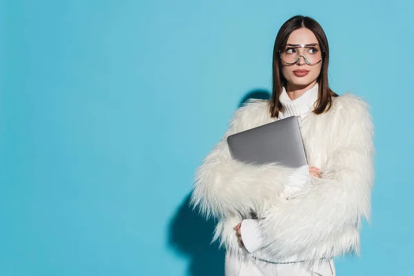 Stylische Frau mit trendiger Brille und stylischer Kunstpelzjacke mit Laptop auf blauem Hintergrund — Stockfoto