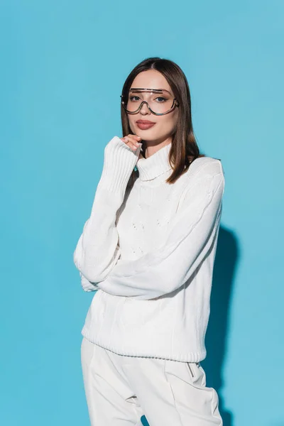 Élégant jeune femme en lunettes et col roulé blanc regardant caméra sur bleu — Photo de stock