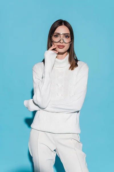 Jolie jeune femme en lunettes et col roulé blanc regardant caméra sur bleu — Photo de stock