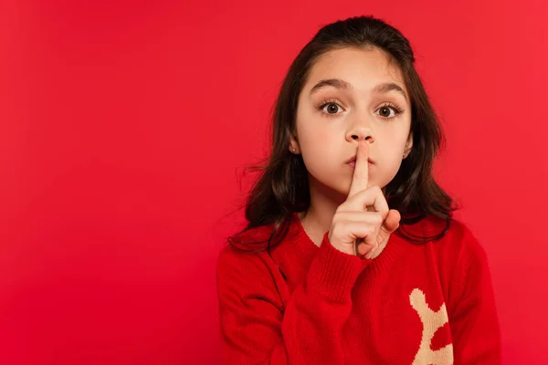 Kind im Winterpullover zeigt Schweigezeichen und blickt vereinzelt in die Kamera auf Rot — Stockfoto