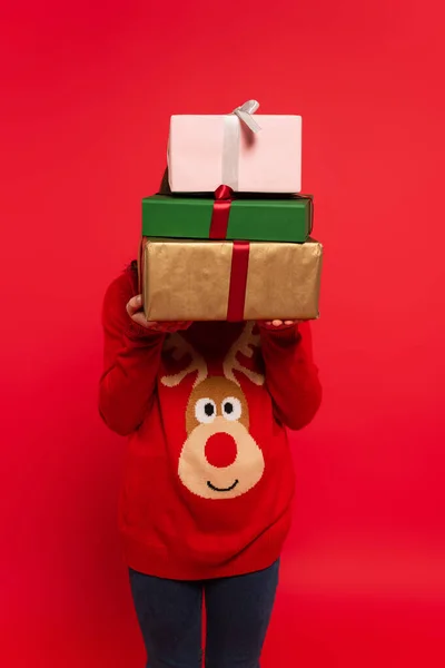 Дитина взимку светр тримає купу різдвяних подарунків ізольовано на червоному — стокове фото
