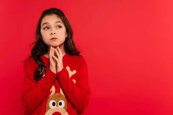 Pensive child in knitted winter sweater looking away isolated on red — Stock Photo