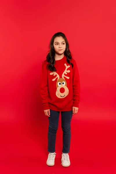 Full length of puzzled kid in winter sweater looking away on red — Stock Photo
