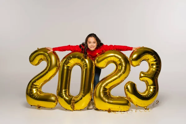 Comprimento total da criança alegre em balões de abraço de camisola vermelha com números 2023 em cinza — Fotografia de Stock