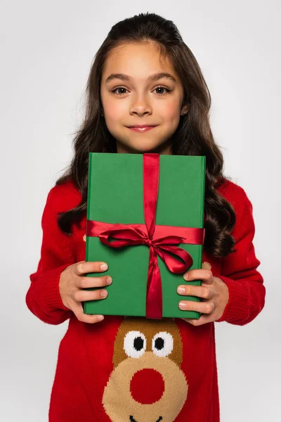 Щаслива дівчина в червоному светрі тримає загорнутий різдвяний подарунок ізольовано на сірому — стокове фото