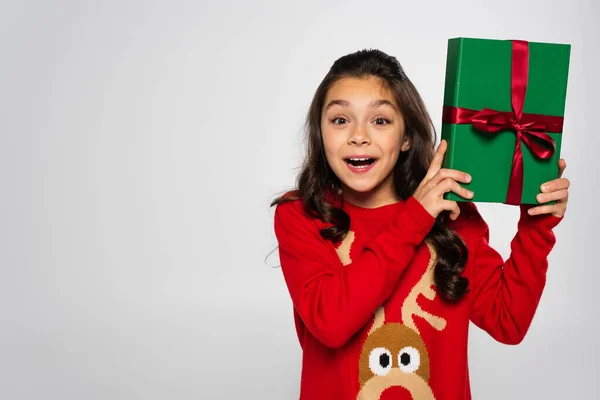 Erstaunt Mädchen in rotem Pullover hält verpacktes Weihnachtsgeschenk isoliert auf grau — Stockfoto