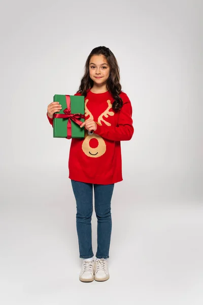 Full length of kid in red sweater holding wrapped Christmas present on grey — Stock Photo