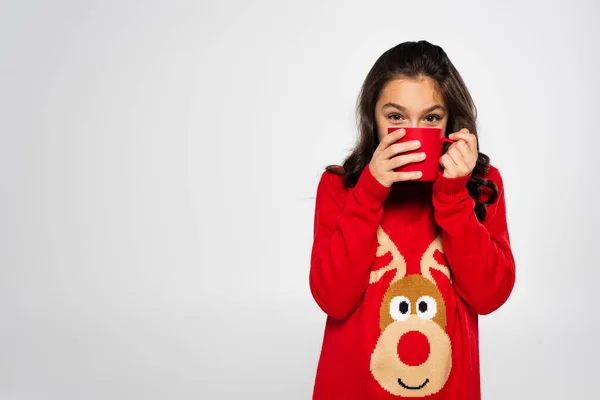Kid in new year sweater with deer print holding cup near face isolated on grey — Stock Photo