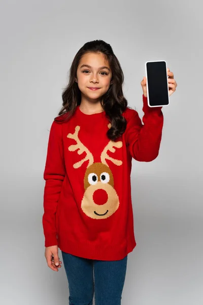 Preteen girl in Christmas sweater holding smartphone isolated on grey — Stock Photo