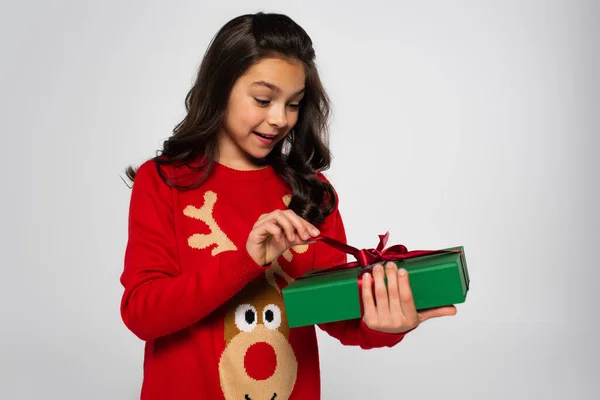 Aufgeregtes Kind im Pullover hält Weihnachtsgeschenk mit Schleife auf Grau — Stockfoto