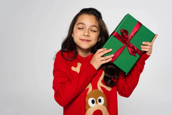Pleased child in red sweater holding Christmas gift isolated on grey — Stock Photo