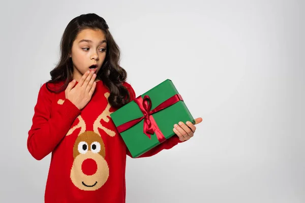 Schockiertes Kind in rotem Pullover hält Geschenkbox isoliert auf grau — Stockfoto