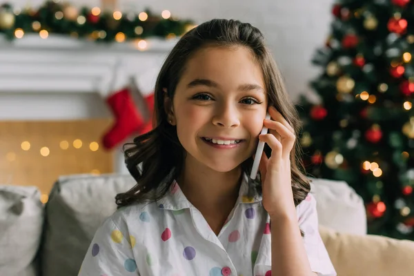 Веселый ребенок в пижаме разговаривает по смартфону во время празднования дома — стоковое фото
