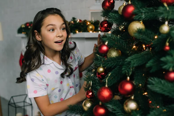 Muchacho emocionado en pijama mirando el árbol de Navidad decorado en casa - foto de stock