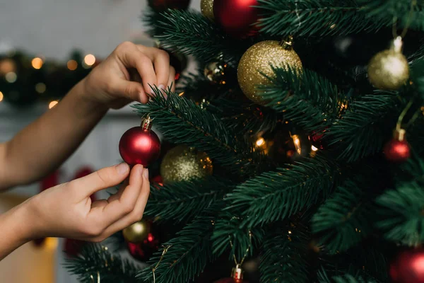 Cropped view of child decorating pine tree with Christmas ball at home — Stock Photo