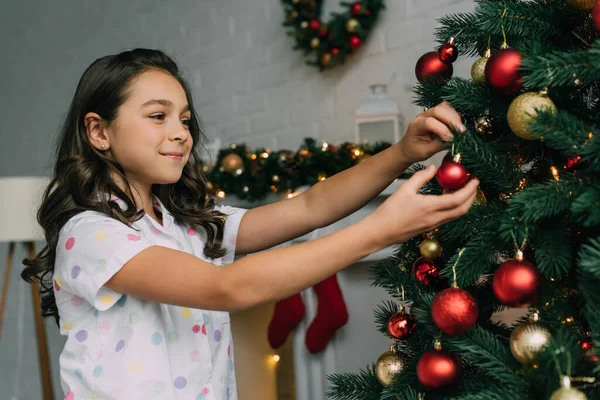Lächelndes Mädchen schmückt Weihnachtsbaum im Wohnzimmer — Stockfoto